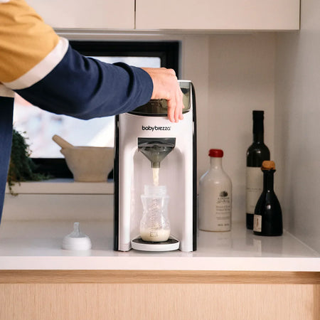 Person using Baby Brezza Formula Pro Advanced on a kitchen counter with bottles in the background