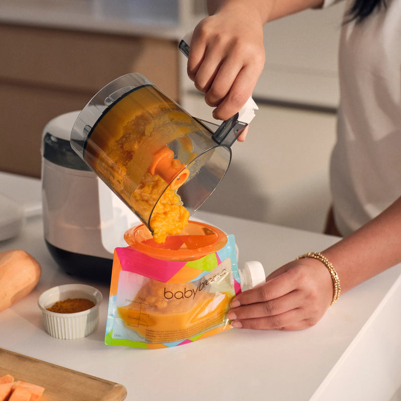 Person using the baby brezza one step baby food maker deluxe to prepare baby food on a kitchen counter.