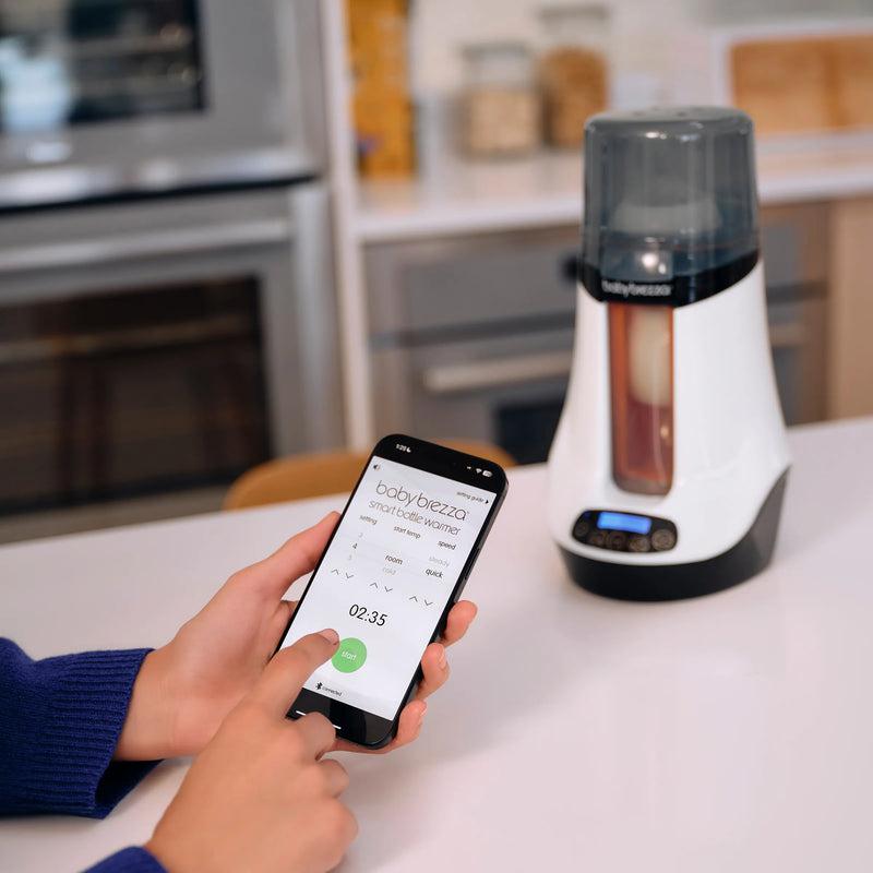 Person using a smartphone app to control the baby brezza smart bottle and breastmilk warmer on a kitchen counter.