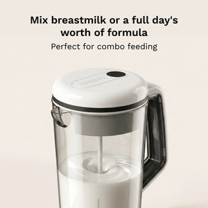 A clear blending pitcher with a white lid and gray handle, shown on a light beige background with text reading 'Mix breastmilk or a full day's worth of formula' and 'Perfect for combo feeding.'.