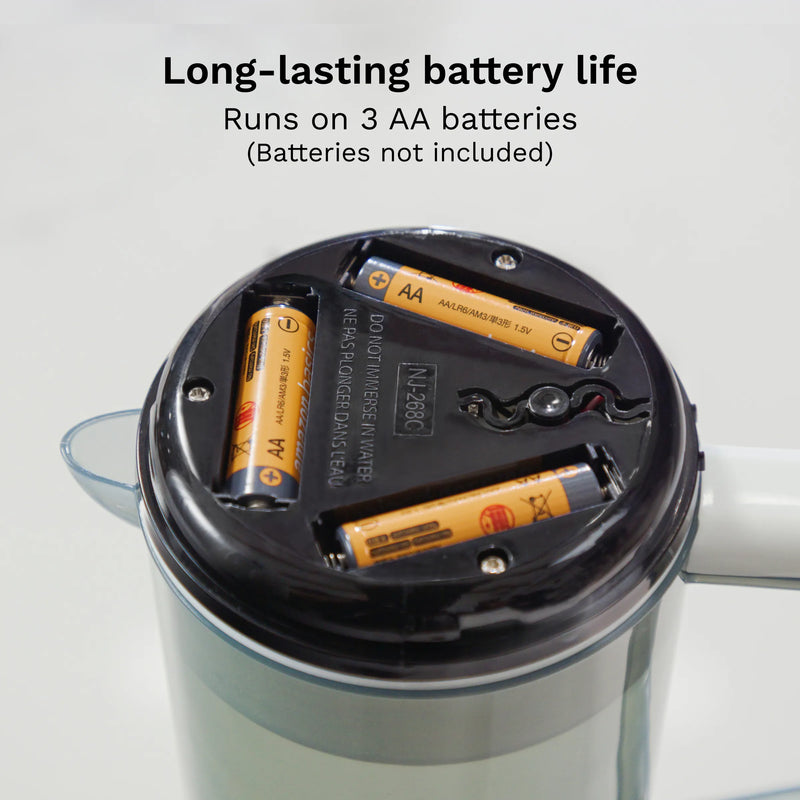 Close-up of a battery compartment inside the Baby Brezza mixing pitcher, showing three AA batteries inserted into the slots. Text at the top reads 'Long-lasting battery life' and 'Runs on 3 AA batteries (Batteries not included)'.