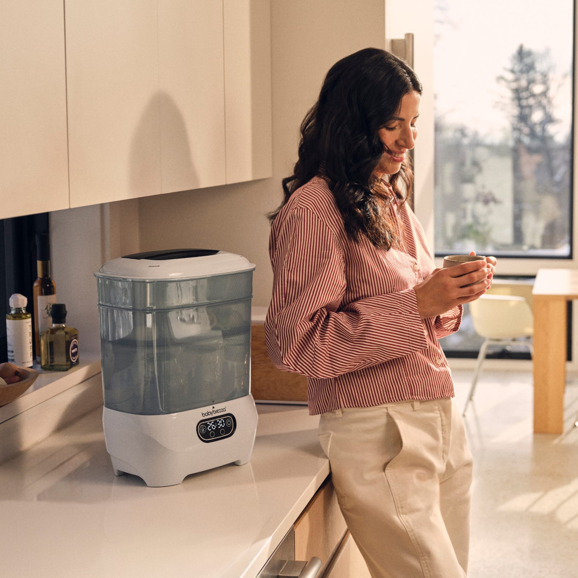 Woman standing in a kitchen with the baby brezza sterilizer dryer advanced on the counter