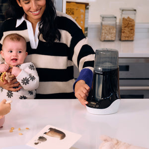 Woman holding a baby and using the baby brezza bottle and breastmilk warmer in a kitchen.