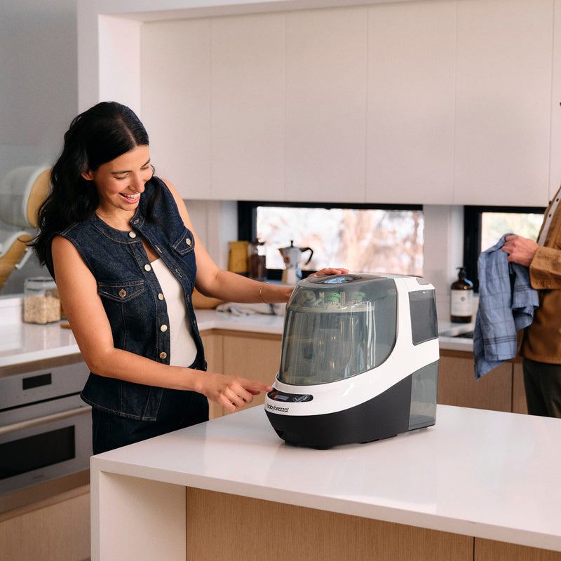 Woman using the baby brezza bottle washer pro on a kitchen island countertop