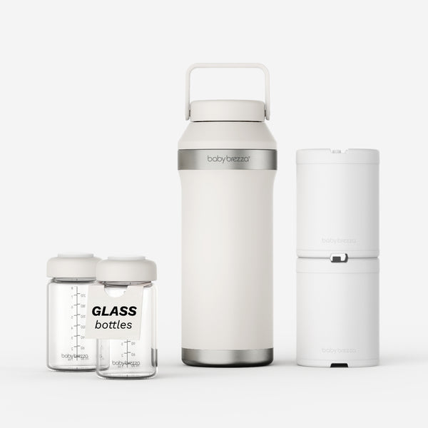 Baby bottle storage set including a tall insulated bottle with handle, two clear glass bottles, and a white cylindrical container, shown on a light gray studio background. The bottle and containers show the Baby Brezza brand.