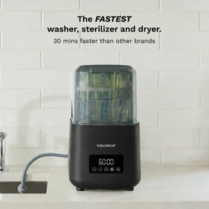 A countertop body brezza instant washer, sterilizer and dryer machine in black with a clear top, set against a white subway tile wall. Text at the top reads 'The FASTEST washer, sterilizer and dryer.