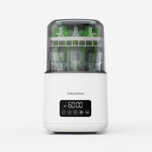 A white Baby Brezza baby washer, bottle sterilizer and dryer shown on a clean white background, with green baby bottles visible inside through a transparent upper chamber.