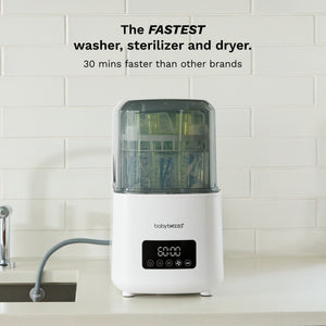 A white Baby Brezza multi-function baby sterilizer, dryer, and washer sits on a kitchen counter with a tiled backsplash. Text at the top reads 'The FASTEST washer, sterilizer and dryer.