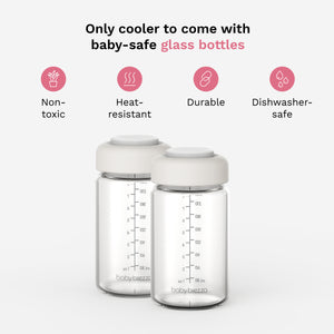 Two clear baby glass bottles with white caps and black measurement markings, shown on a light gray background with marketing text and pink feature icons above them. The visible brand at the bottom of the bottles is Baby Brezza.