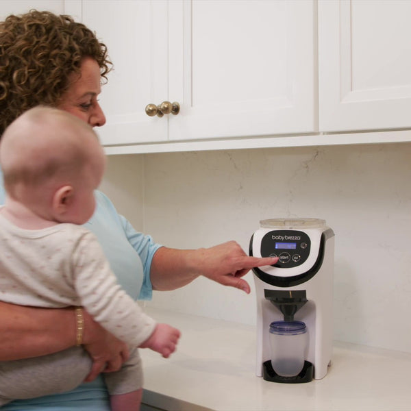 White Formula Pro Mini travel formula dispenser on counter with woman holding a baby operating at it - product thumbnail