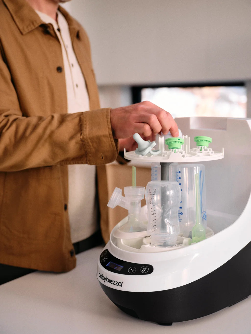Person using Baby Brezza Bottle Washer Pro sterilizer with multiple bottles on a white surface.