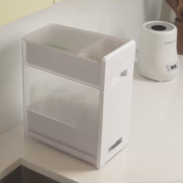 Load video: Upgrade how you dry and store your bottles, pump parts, and accessories with the Baby Brezza Covered Drying Rack and Organizer. Holds up to 8 bottles.  Quick drying with perforated bins. Drip tray slips out easily. Elevate your countertops while keeping your baby products organized, dry, and protected from germs.