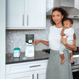 #variant_white Woman holding a baby and using the water warmer for baby